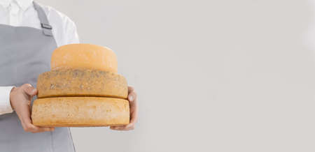 Farmer in gray apron holds homemade round of cheese in wooden boxの写真素材