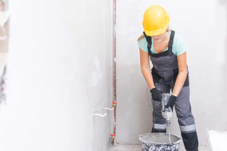 Woman builder worker kneads cement and plaster with mixer to level gray concrete wallsの写真素材