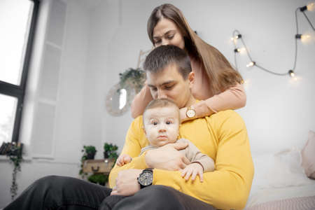 Happy young family woman, man and child are sitting on bed and smiling, light backgroundの写真素材