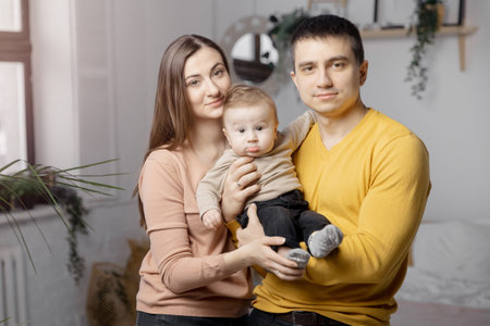 Happy young family woman, man and child are sitting on bed and smiling, light background