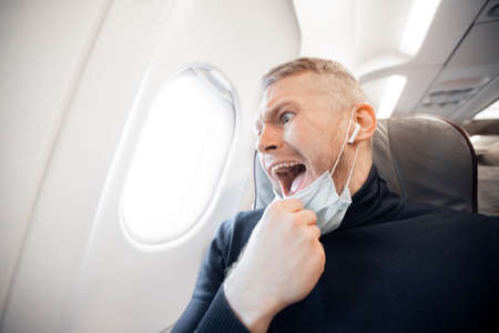 Concept aerophobia or aviophobia. Afraid of fear flying on airplane and height tourist man in safe medical maskの写真素材