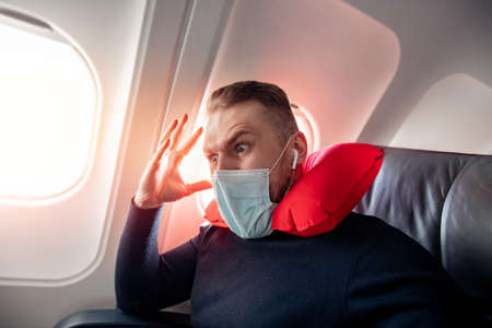 Concept aerophobia or aviophobia. Afraid of fear flying on airplane and height tourist man in safe medical maskの写真素材