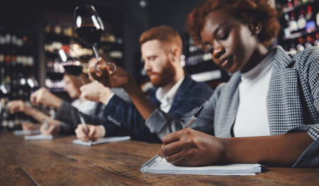 African woman tasting red wine sommeliers and taking notes at degustation notepadの写真素材