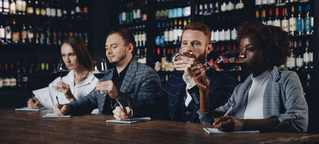 Banner African Woman and caucasian man sommeliers tasting red wine and taking notes at degustation notepadの写真素材