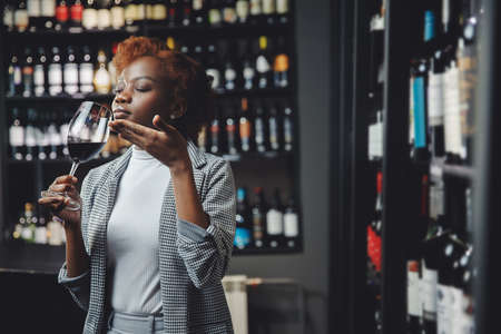 African young woman sommelier holds glass with red wine, buy alcohol at supermarketの写真素材