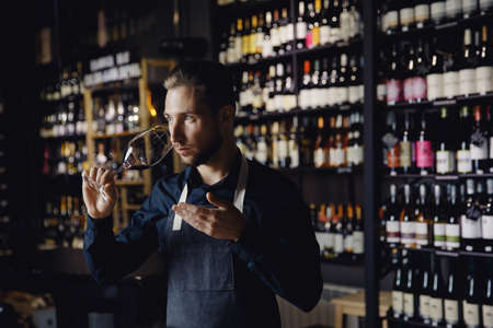 Winemaker sommelier man sniffing aroma red wine in glass background bottles restoranの写真素材