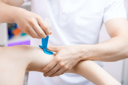 Concept closeup tape kinesio therapy. Doctor physiotherapist rehabilitation of sports pain of hand athlete womanの写真素材