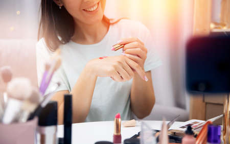 Happy woman vlogger is review cosmetics lipstick recording video stream on phone. Concept Influencer blogger beauty blogの写真素材