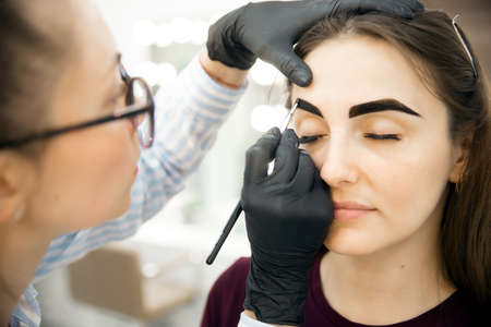 Beauty salon, master corrects and dyes eyebrows hair of young womanの写真素材