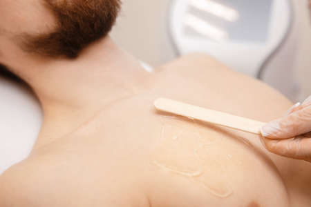 Laser depilation concept for men. Beauty salon worker applies gel to guy body before hair removalの写真素材