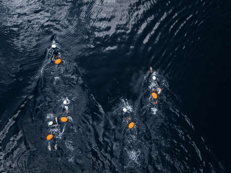 Arctic people swim ice hole in cold water, athletes in wetsuits with orange buoys in blue seaの写真素材