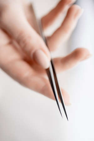 Close-up hand of master holds tools for eyebrow correction and eyelash extension tweezers and tongs on white backgroundの写真素材