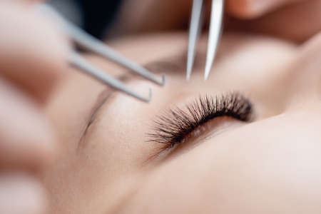 Eyelash extension procedure. Master tweezers black fake long lashes beautiful female eyesの写真素材