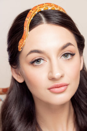 Fashion portrait of young brunette woman with snake on her head, symbol of youth, beauty, skin...