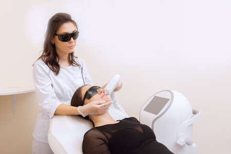 Master carries out removal moustache of unwanted hair laser on face young woman. Health and beauty conceptの写真素材