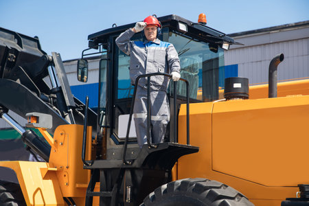 Excavator driver in hard hat stands at construction equipment, concept industrial man portrait