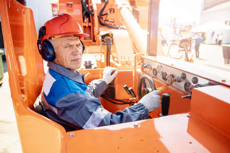 Banner industrial man holding hard hat on background of excavator. Concept of job placement for drivers of construction equipmentの写真素材