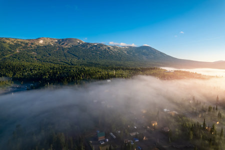 Mountain with visible silhouettes forest tree through morning colorful fog sunrise, aerial top viewの写真素材