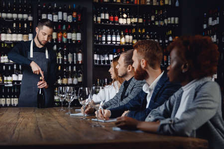 Sommelier training concept, man opens bottle of red wine for tasting for new waitersの写真素材