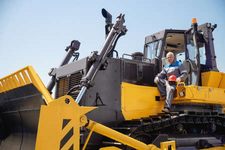 Industrial portrait of working man, excavator driver climbs into cab to perform work on construction siteの写真素材