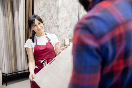 Woman consultant shows laminate flooring to a man in a storeの写真素材