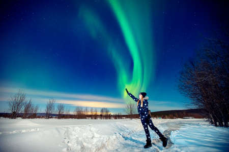 Woman tourist looks aurora northern lights night at forest, soft focusの写真素材