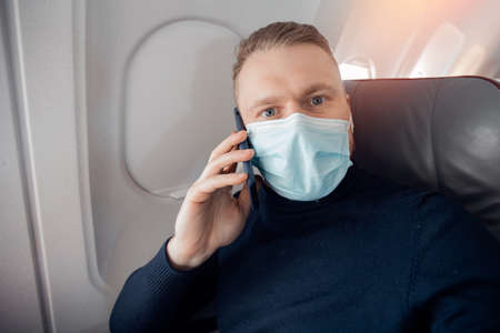 Male with safe mask passenger of airplane talking on cell phone in chair. Concept travel covidの写真素材
