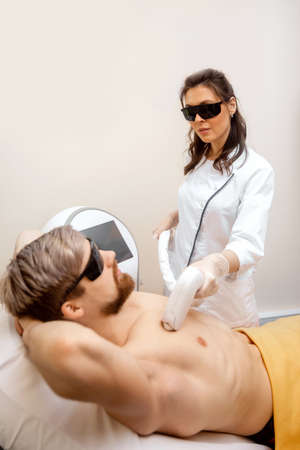 Woman worker beauty salon giving man torso hair removal laser epilation studioの写真素材