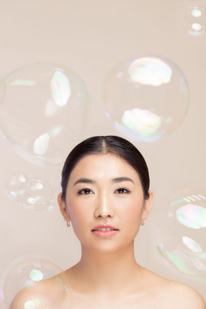 Fashion portrait of asian woman on light studio background with soap bubbles, fake eyelashes and...