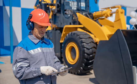 Industrial mechanic uses tablet test online status of bulldozer at construction site. Concept optimization of work of business processes in buildingの写真素材