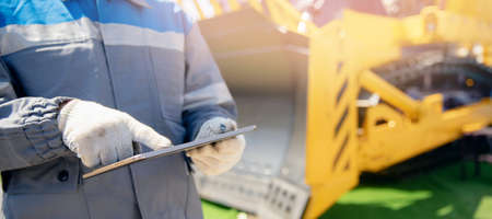 Banner industrial senior engineer in hardhat is using tablet computer in construction site background bulldozer, sunlightの写真素材