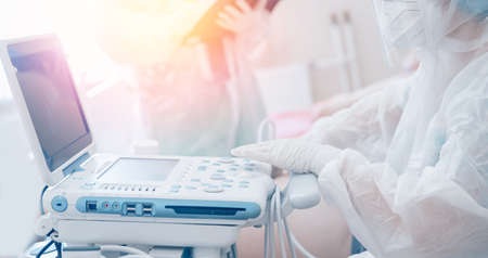 Nurse wearing protective suit and mask uses ultrasound machine on patient with positive coronavirus test. Pandemic analysis conceptの写真素材