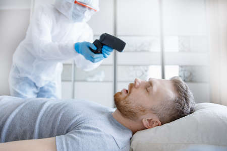 Measurement of temperature in coronavirus patient. Doctor measures man with thermometer and makes treatmentの写真素材