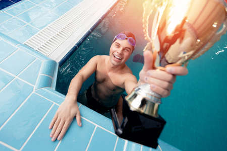 Concept swimming competition, happy young man winner swimmer holding trophyの写真素材