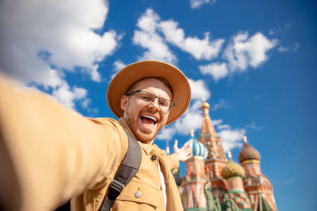 Young man traveler in brown hat makes selfie photo on background of Kremlin red square. Concept travel to Russiaの写真素材