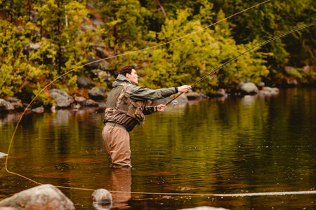 Fisherman using rod fly fishing in mountain river autumn splashing waterの写真素材