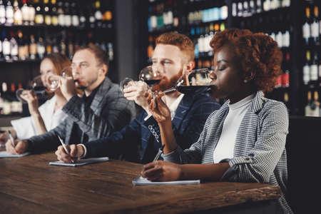 African Woman and caucasian man sommeliers tasting red wine and taking notes at degustation notepadの写真素材