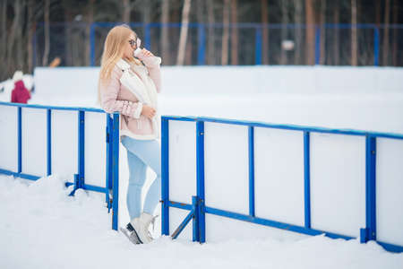 Young woman drinks hot tea or coffee from vacuum flask on skating rink in winterの写真素材