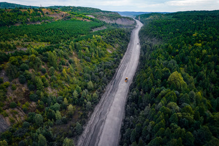 Large yellow truck rides through forest to be loaded into open coal mine