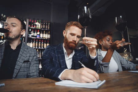 Friends tasting red wine sommeliers and taking notes at degustation notepadの写真素材