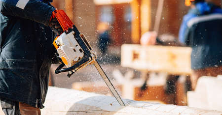 Industrial work carpenter sawing with chainsaw log, construction frame building site of house made of woodの写真素材