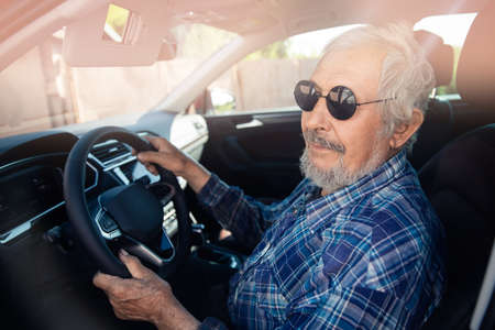 Old man pensioner in round sunglasses driving carの写真素材