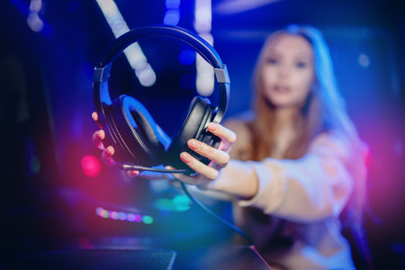 Woman hand hold headphones with microphone for video games and cyber sports on neon background