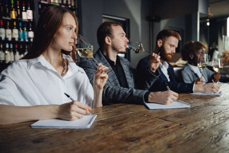 Sommeliers female and male tasting white wine and making notes at degustation card notepadの写真素材