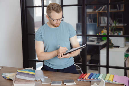 Tailor man chooses material and color of upholstery of upholstered furniture at workplace. Apartment renovation project design conceptの写真素材