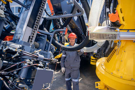 Engineer in hard hat and uniform is servicing hydraulic systems of mining equipment for descending into mineの写真素材