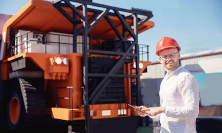 Young man engineer in helmet with tablet computer in hands on background of truck for coal mining oreの写真素材