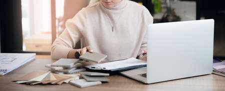 Banner Interior designer workplace. Woman work laptop, tile sets and colored set of fabrics for furnitureの写真素材