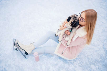 Young woman goes in for winter sports on rink skates with pug dogの写真素材