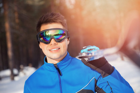 Portrait of racer male skier with cross country skis on background of winter forest